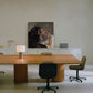 A large square wall art print depicting a black bear and a leopard, displayed in a modern minimalist office setting above a wooden conference table and chairs.