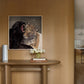 A framed art print depicting a black panther and a leopard, displayed on a curved wooden wall above a matching wooden console table with a vase of white flowers.