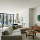 Modern living room with gray sectional sofa, wooden coffee table, and kitchen in the background.