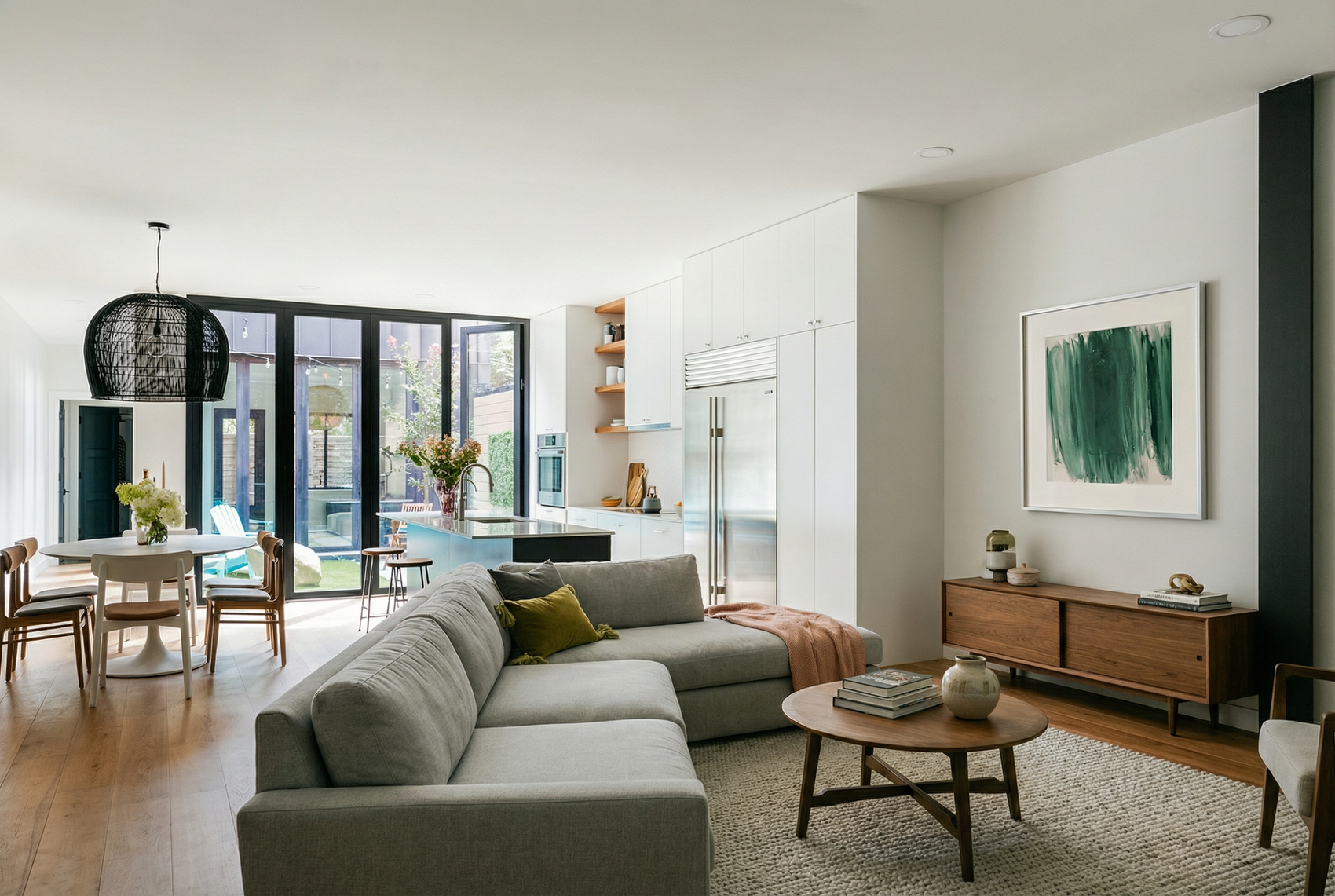 Modern living room with gray sectional sofa, wooden coffee table, and kitchen in the background.