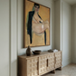 Large painting of a nude figure on a wall above a wooden sideboard with decorative items. Girl with Short Hair – Portrait Canvas Art | Luxury Wall Decor | Brume Art
