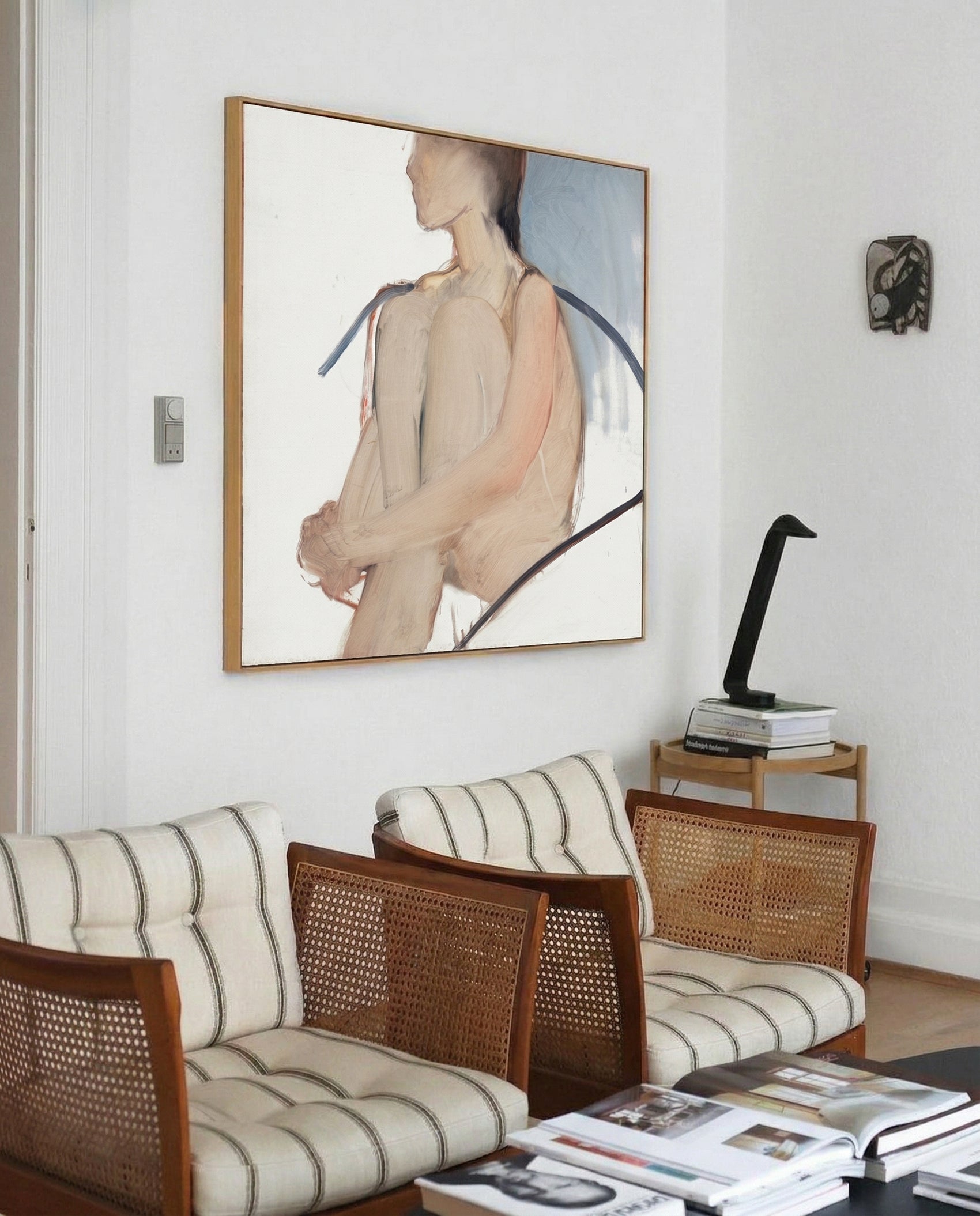 Living room with wicker furniture, striped cushions, and a large framed painting on the wall. Held body – Figurative Canvas Wall Art | Contemporary Luxury Print | Brume Art