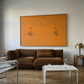 Modern living room with a brown sofa, white coffee table, and orange abstract art on the wall. Marks – Bold Abstract Canvas Wall Art | Premium Luxury Print | Brume Art