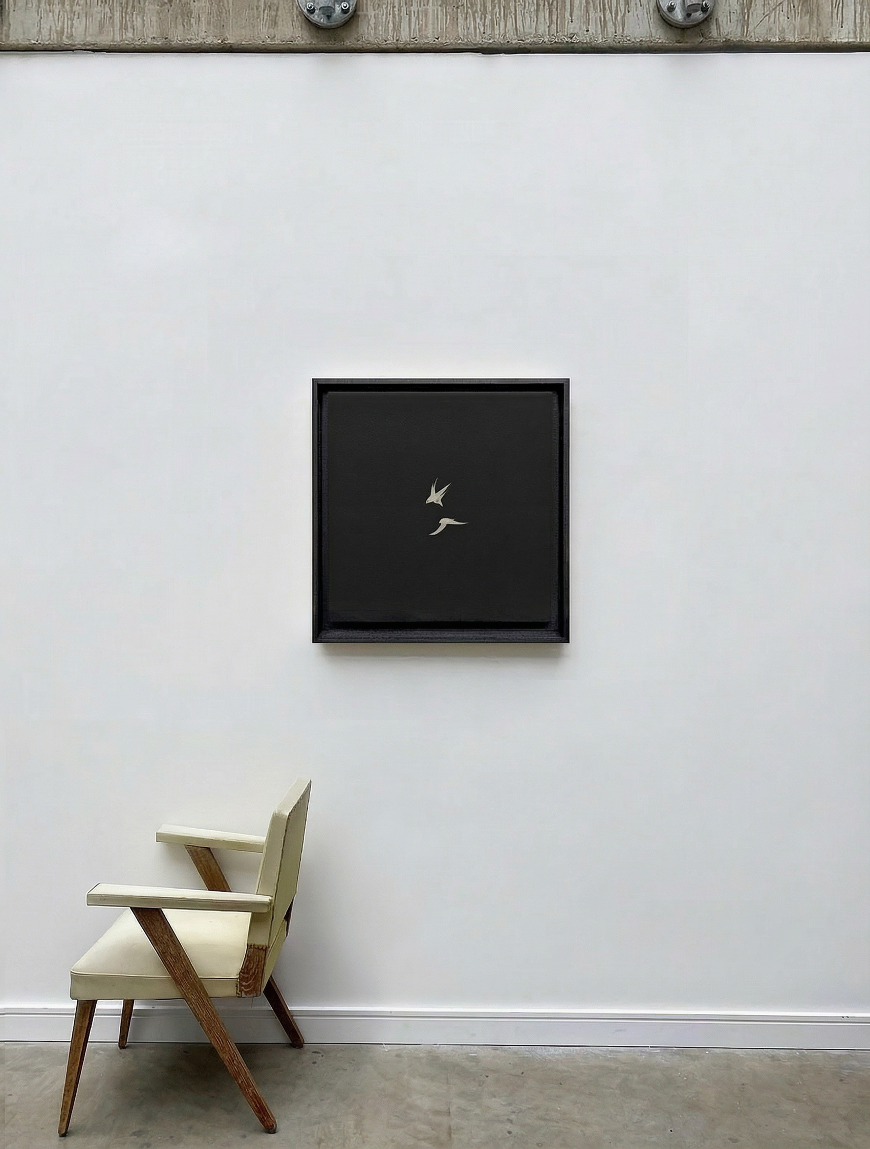 Minimalist black-framed artwork on a white wall with a chair below.Bird 2 – Elegant Nature Canvas Print | Luxury Wall Art | Brume Art