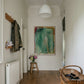 Narrow hallway with a coat rack, radiator, and abstract painting on a white wall. Abstract painting with green and brown tones on a white background Field green 2 – Abstract Canvas Wall Art | Large Luxury Print | Brume Art