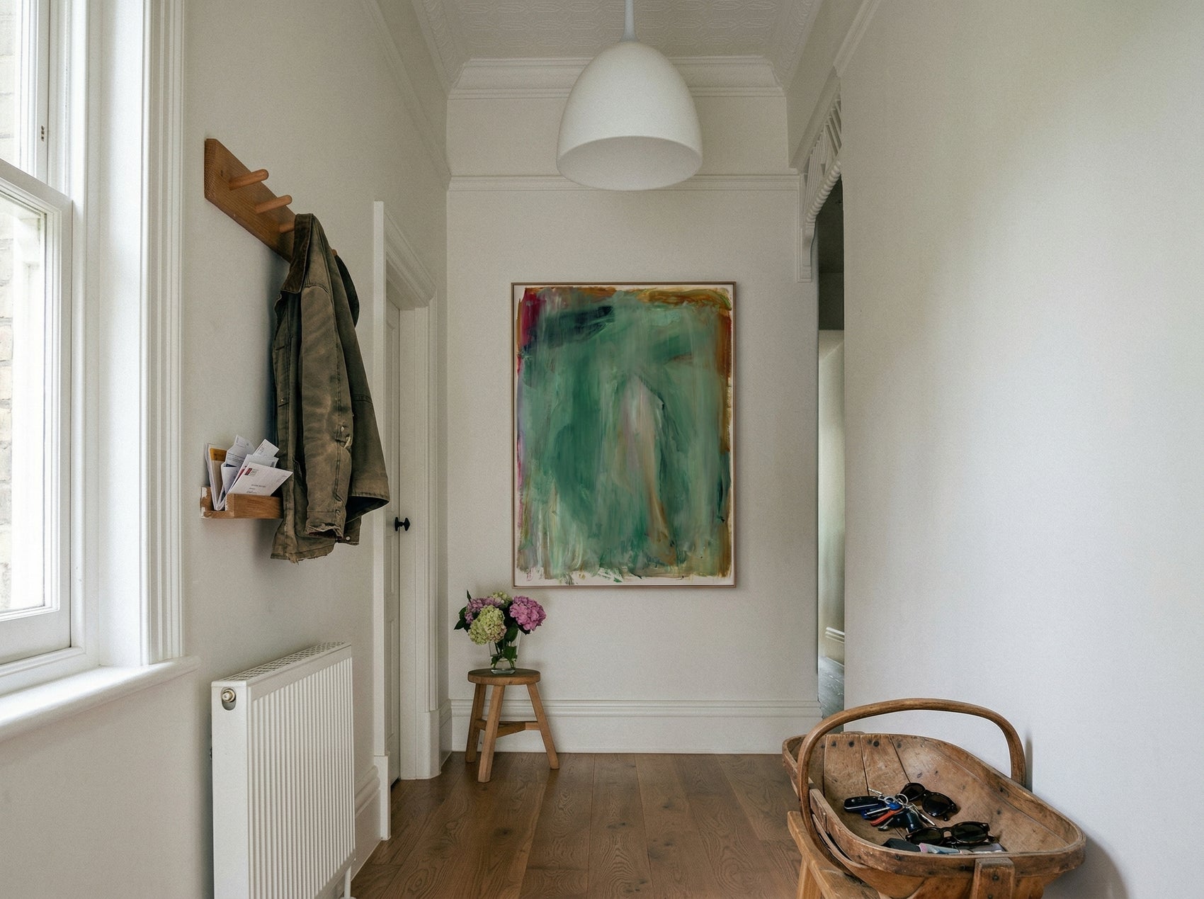 Narrow hallway with a coat rack, radiator, and abstract painting on a white wall. Abstract painting with green and brown tones on a white background Field green 2 – Abstract Canvas Wall Art | Large Luxury Print | Brume Art