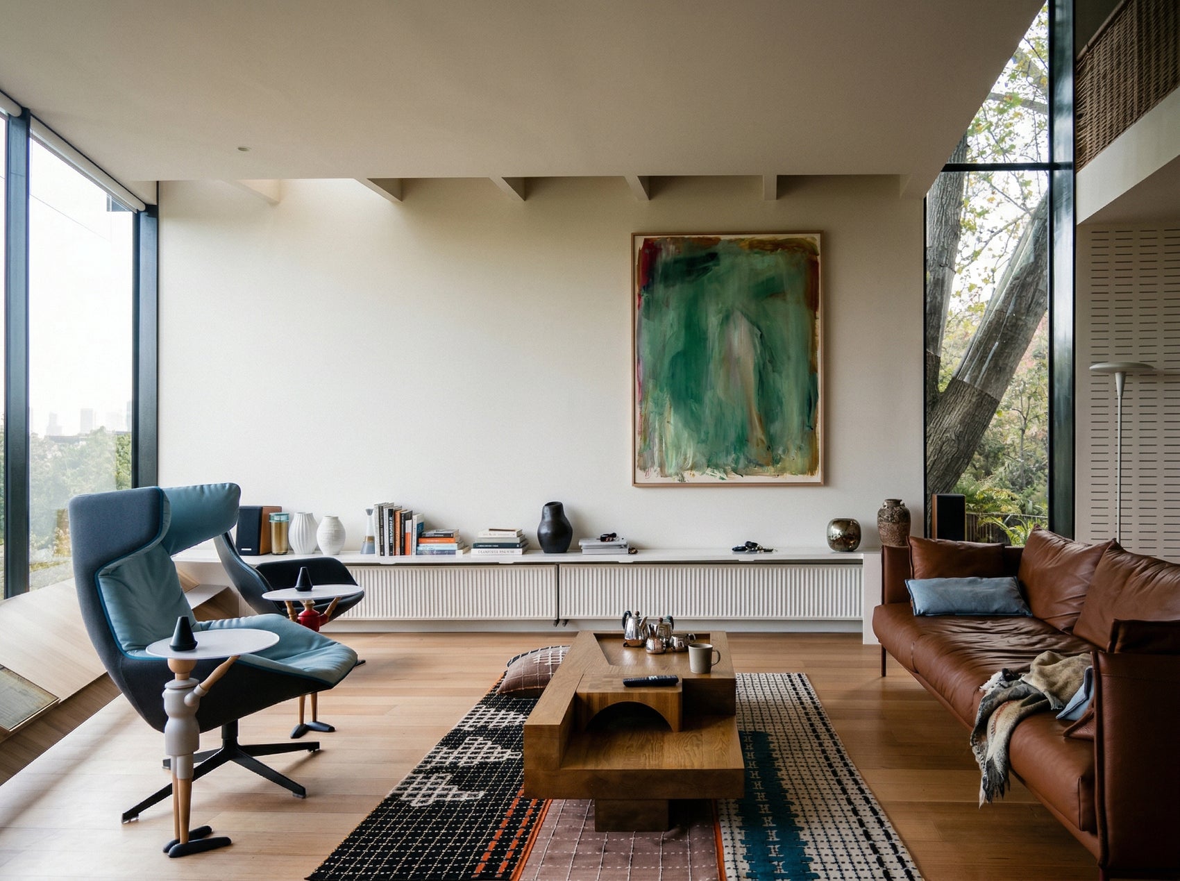 Modern living room with a brown sofa, blue armchair, and abstract painting on the wall. Abstract painting with green and brown tones on a white background Field green 2 – Abstract Canvas Wall Art | Large Luxury Print | Brume Art