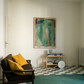 Living room with a dark sofa, yellow cushions, a checkered floor, and a large abstract painting on the wall. Abstract painting with green and brown tones on a white background Field green 2 – Abstract Canvas Wall Art | Large Luxury Print | Brume Art