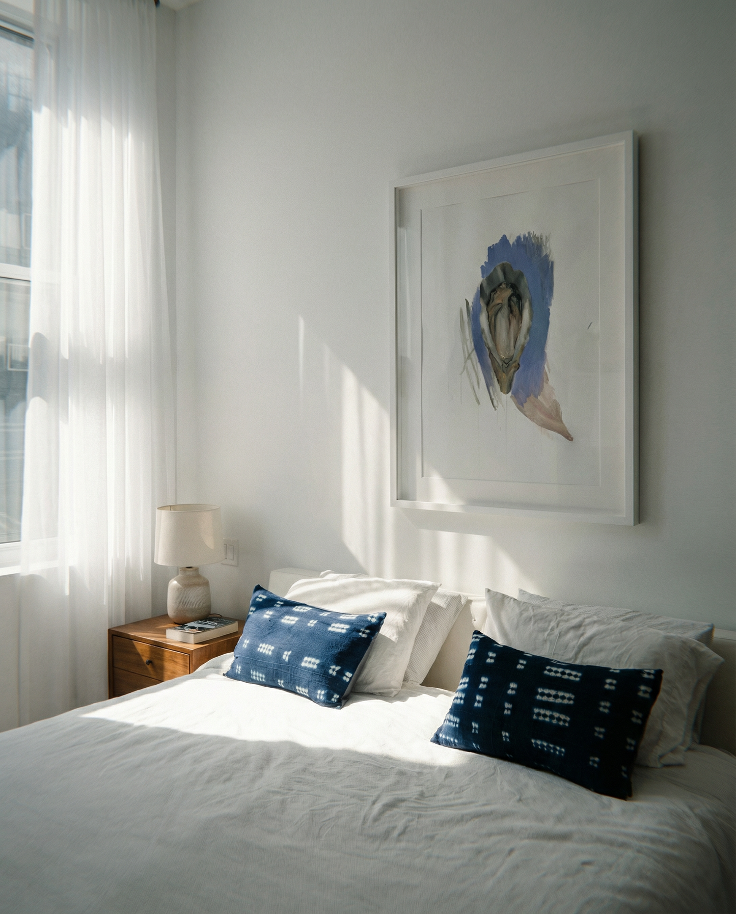 Bedroom with white bedding and blue pillows, framed artwork on the wall. oyster – Elegant Abstract Canvas Wall Art | Luxury Giclée Print | Brume Art| Luxury Wall Decor | Large Canvas Wall Art | Oversized Wall Hanging-Brume art