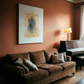 Brown sofa with cushions in a room with a painting and lamp on an orange wall. Fading figure – Bold Abstract Canvas Print | Large Luxury Wall Art | Brume Art