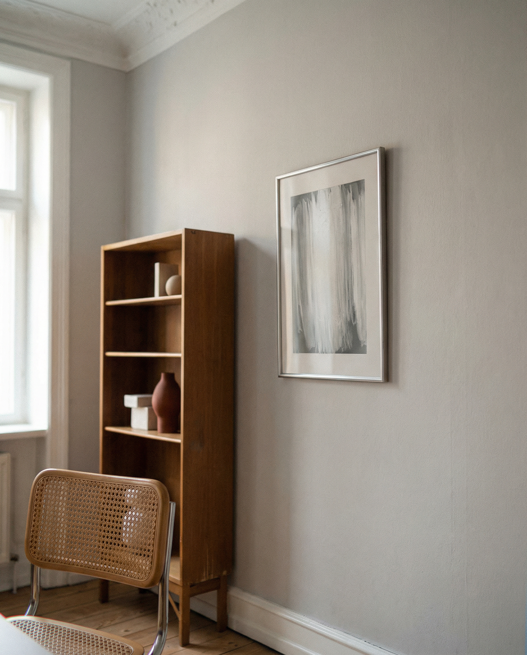Wooden bookshelf with decorative items next to a wall with a framed picture in a room with natural light. fade 4– Bold Abstract Canvas Print | Large Luxury Wall Art | Brume Art| Luxury Wall Decor | Large Canvas Wall Art | Oversized Wall Hanging-Brume art