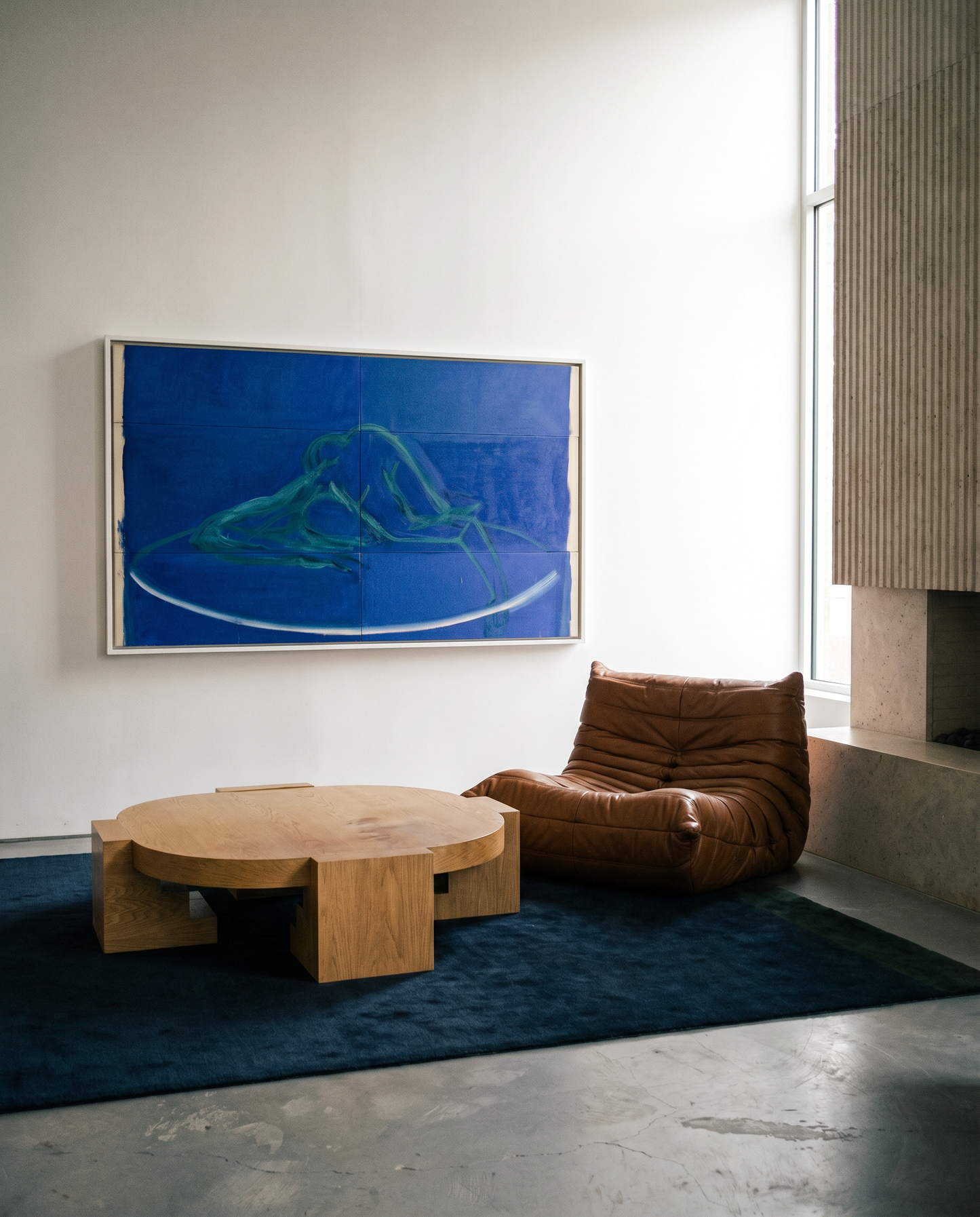 Modern living room with a brown leather chair, wooden coffee table, and abstract blue painting on the wall.