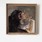 A framed painting depicting a black panther roaring next to a leopard with a white cloth draped over its shoulder, hung on a plain white wall.