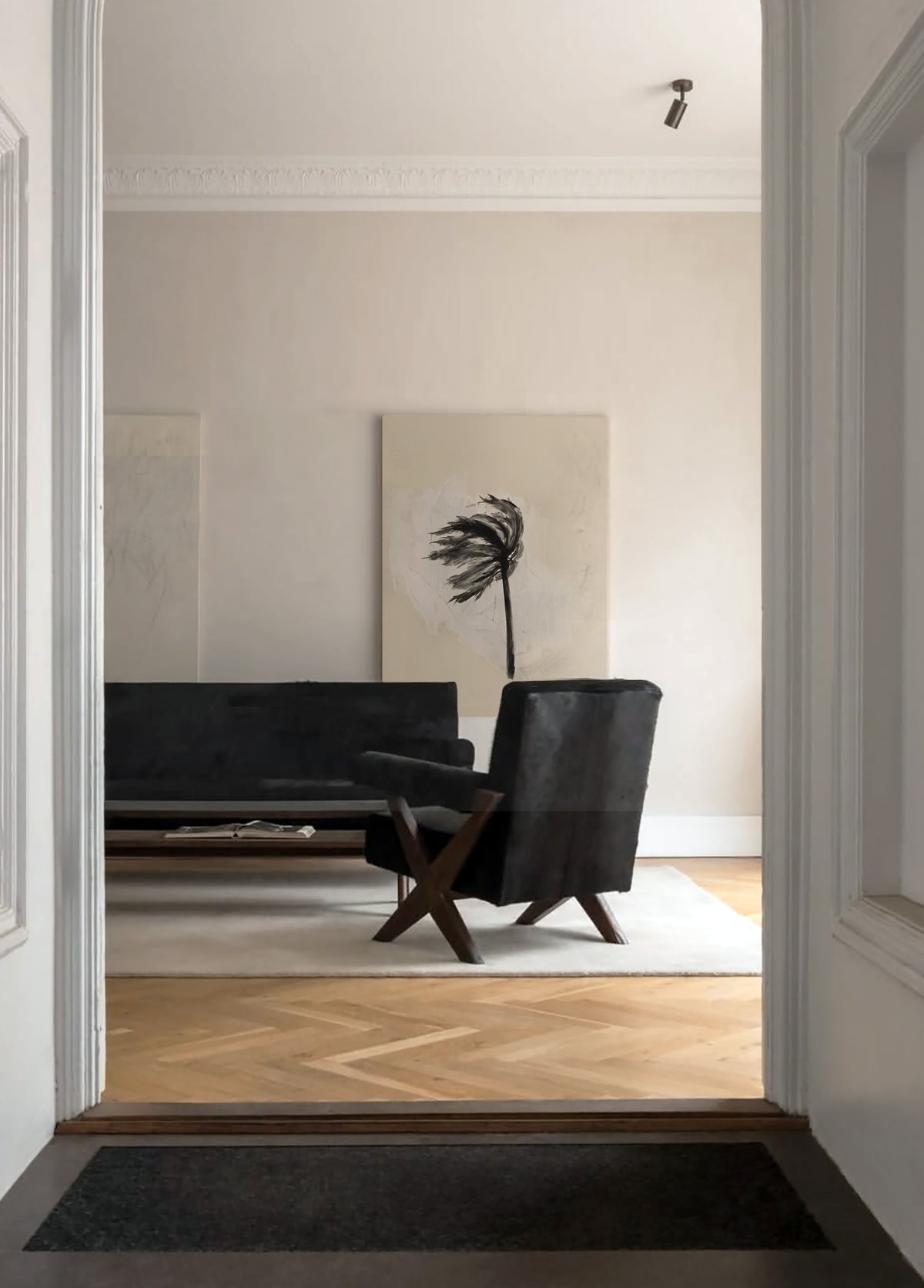 A modern interior scene viewed through a doorway, showing a black armchair and a black sofa in a minimalist living room with light wood flooring and a large abstract wall art piece.