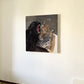 A square canvas painting of a black panther roaring at a leopard, displayed on an off-white wall in an indoor setting.