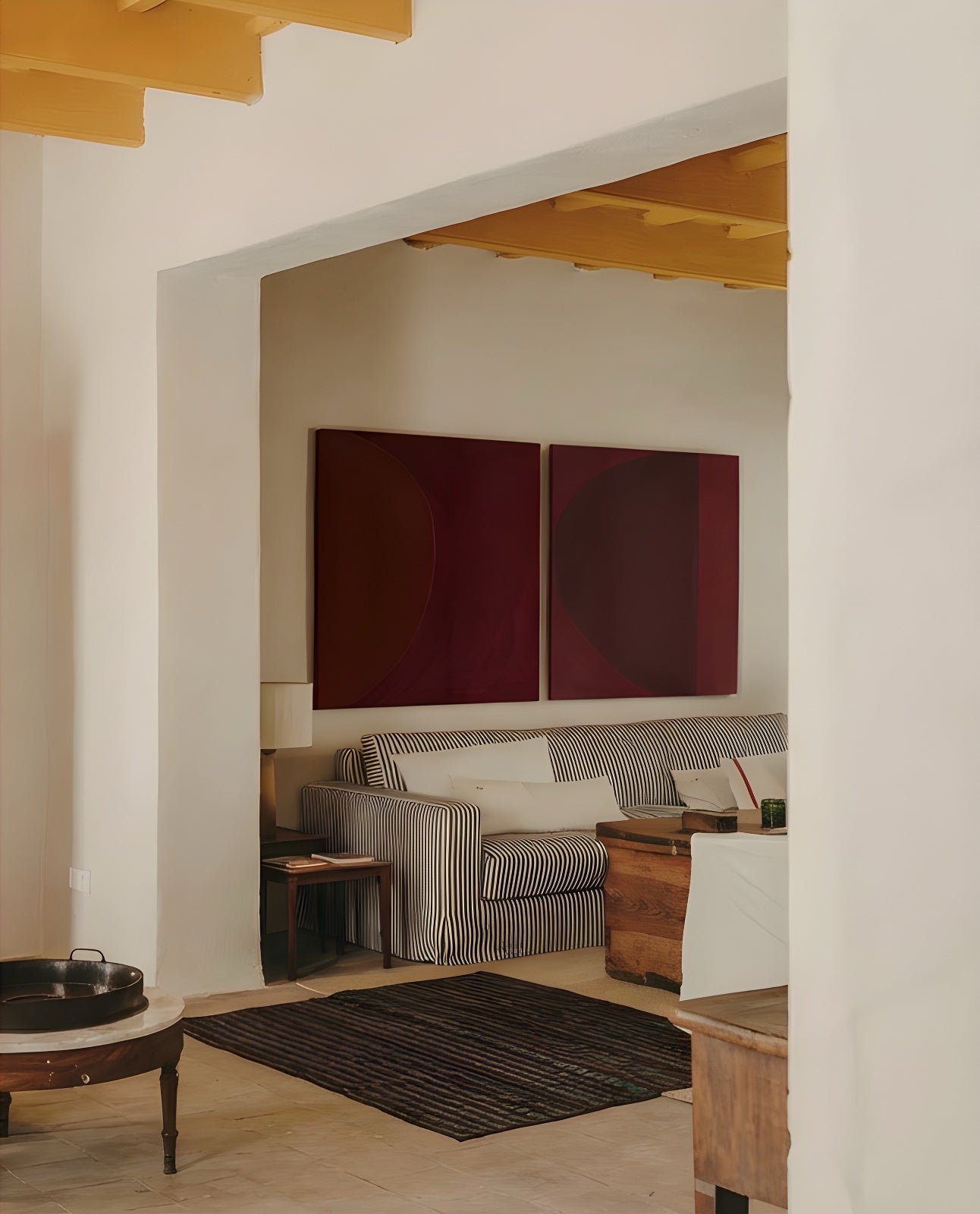 Living room with a striped sofa, wooden coffee table, and two red abstract paintings on the wall. Eclipse – Contemporary Abstract Canvas | Oversized Luxury Wall Art | Brume Art