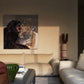 A square canvas painting of a leopard and a black cat hanging on a beige wall in a modern living room setting with a cream sofa and a gray coffee table.