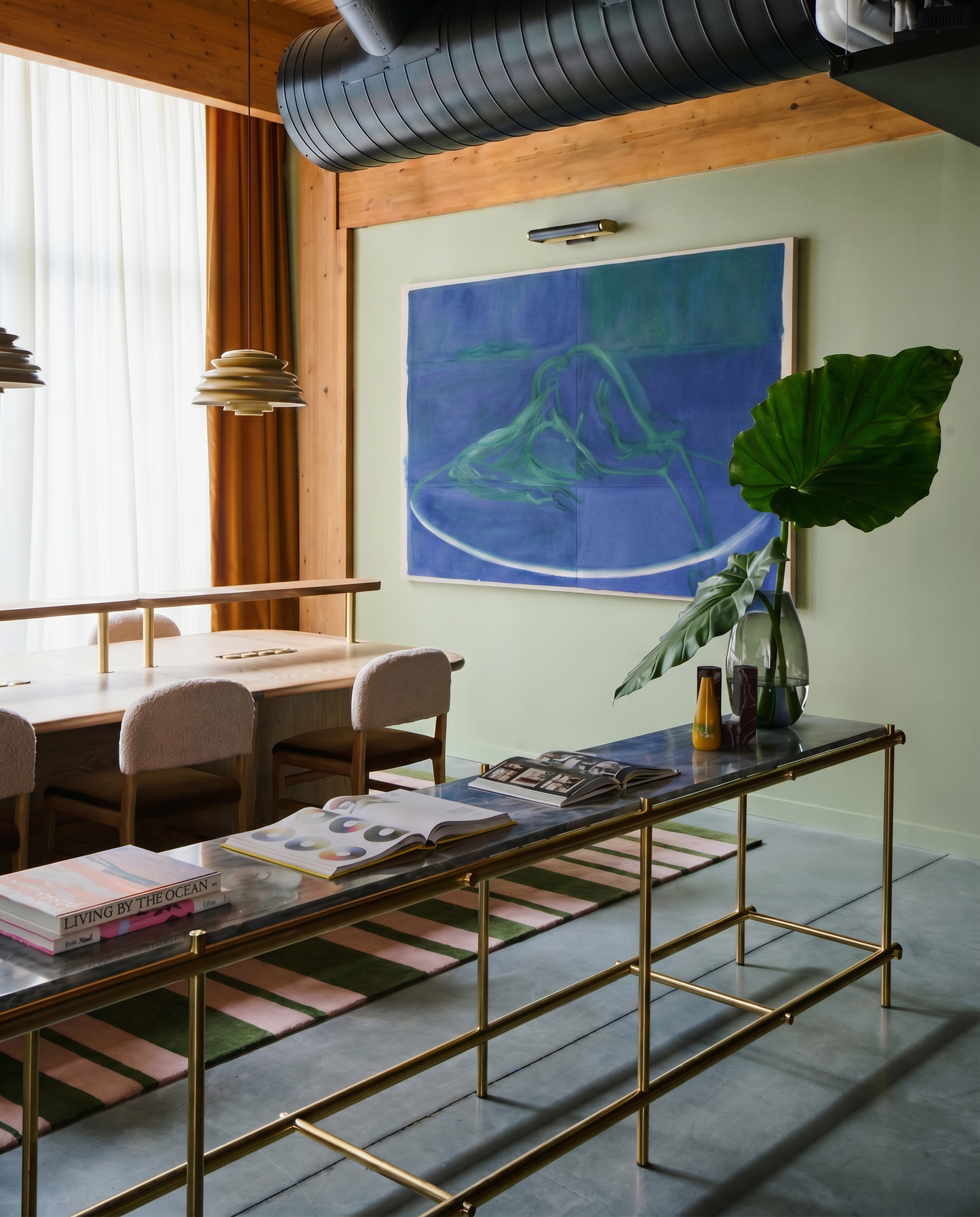 Modern interior with a gold console table, books, and a painting on a green wall.