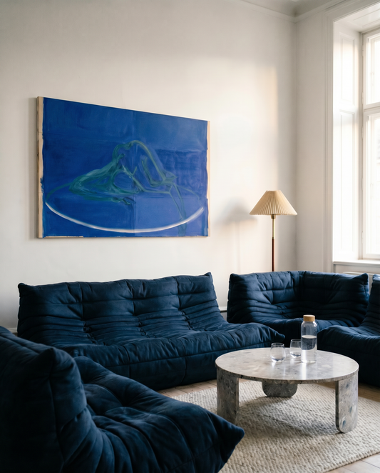 Modern living room with dark blue sofa, abstract painting, and marble coffee table.