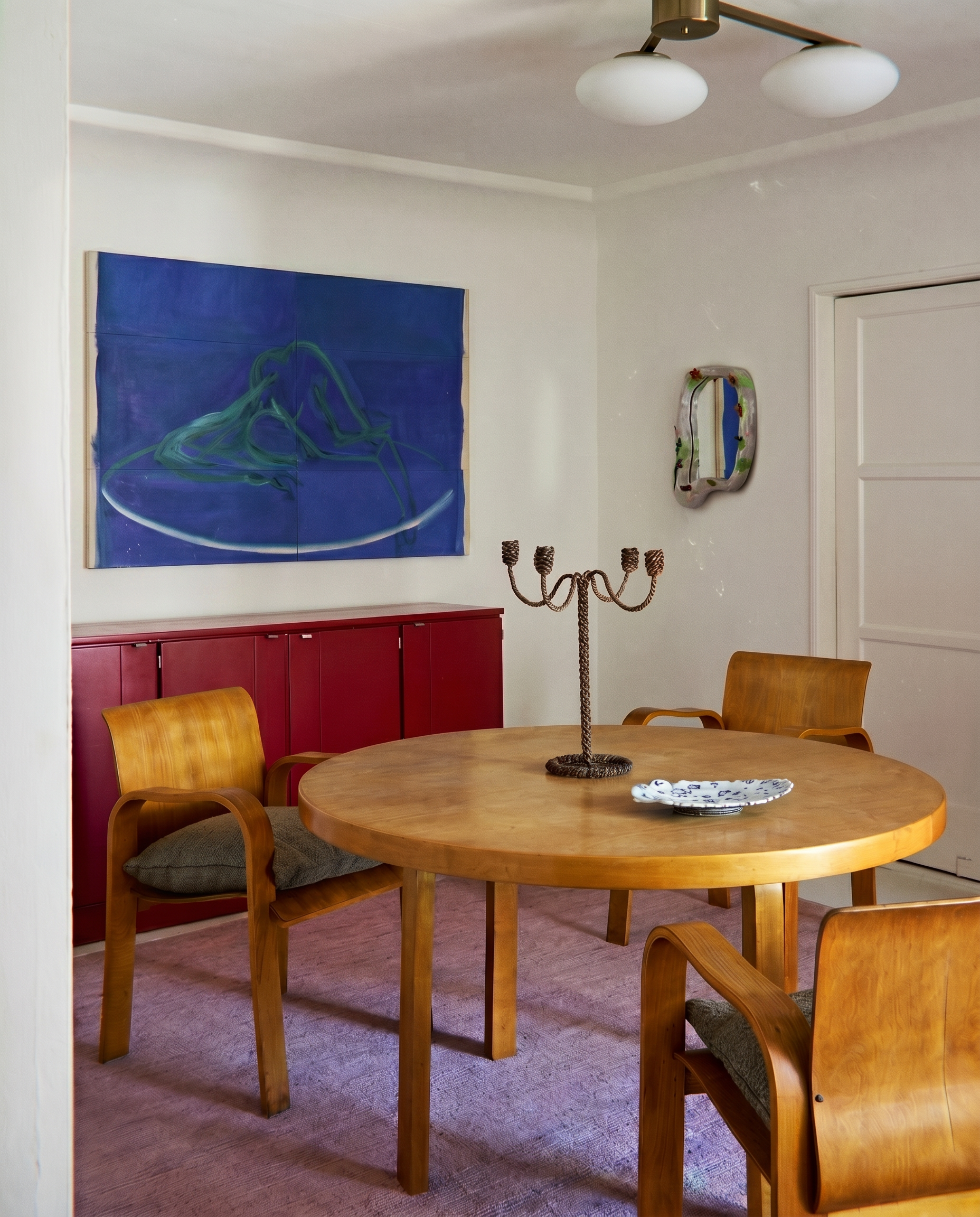 Dining room with wooden table and chairs, red cabinet, and abstract art on the wall.