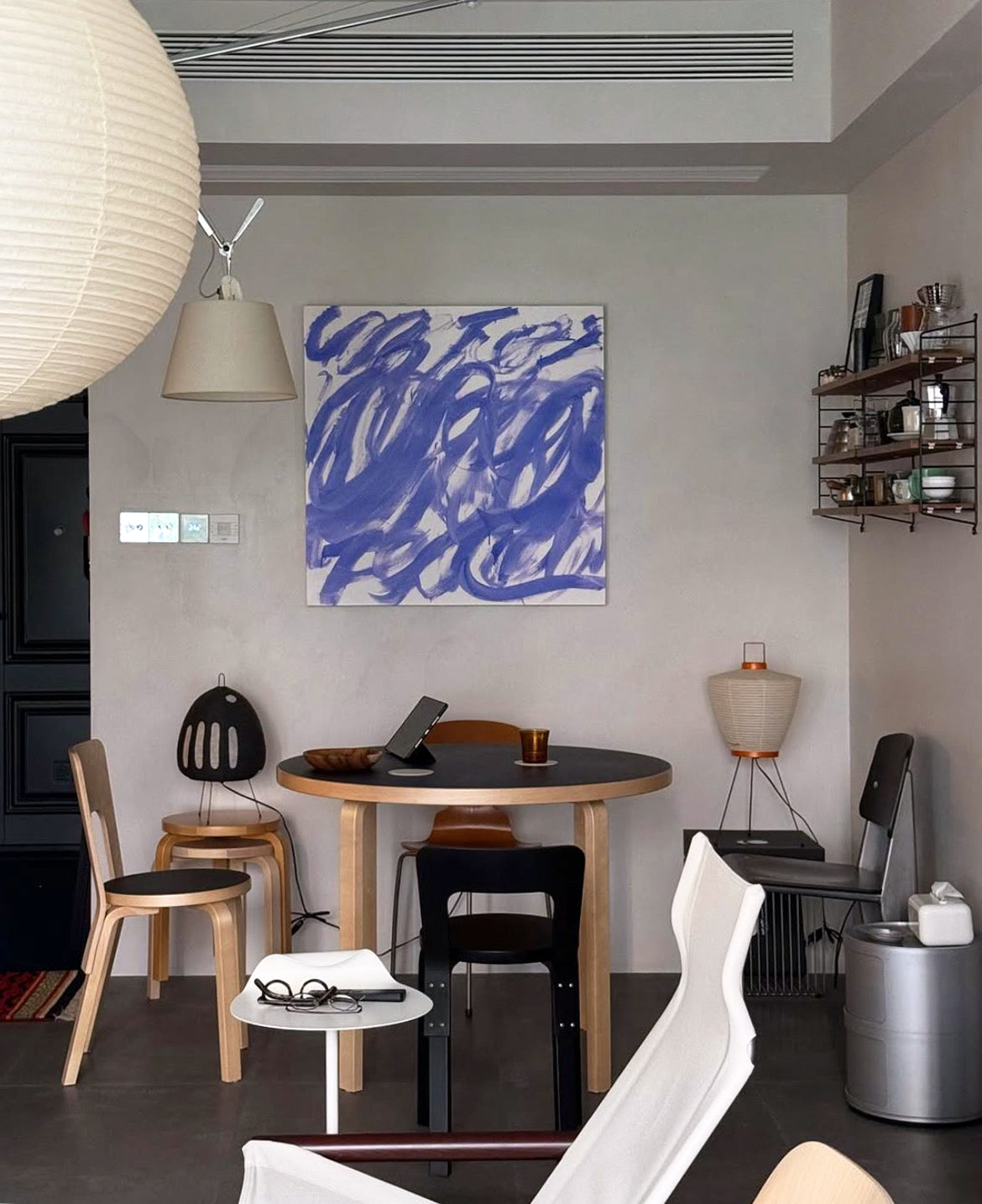 Modern dining room with a round table and chairs, abstract blue painting on the wall, and decorative items. Noise 3 – Textured Abstract Canvas Art | Premium Luxury Wall Decor | Brume Art | Luxury Wall Decor | Large Canvas Wall Art | Oversized Wall Hanging-Brume art