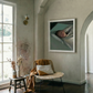 Cozy living room with a wicker chair, small table, and framed artwork on the wall. Gaze – Figurative Canvas Wall Art | Premium Luxury Print | Brume Art | Luxury Wall Decor | Large Canvas Wall Art | Oversized Wall Hanging-Brume art